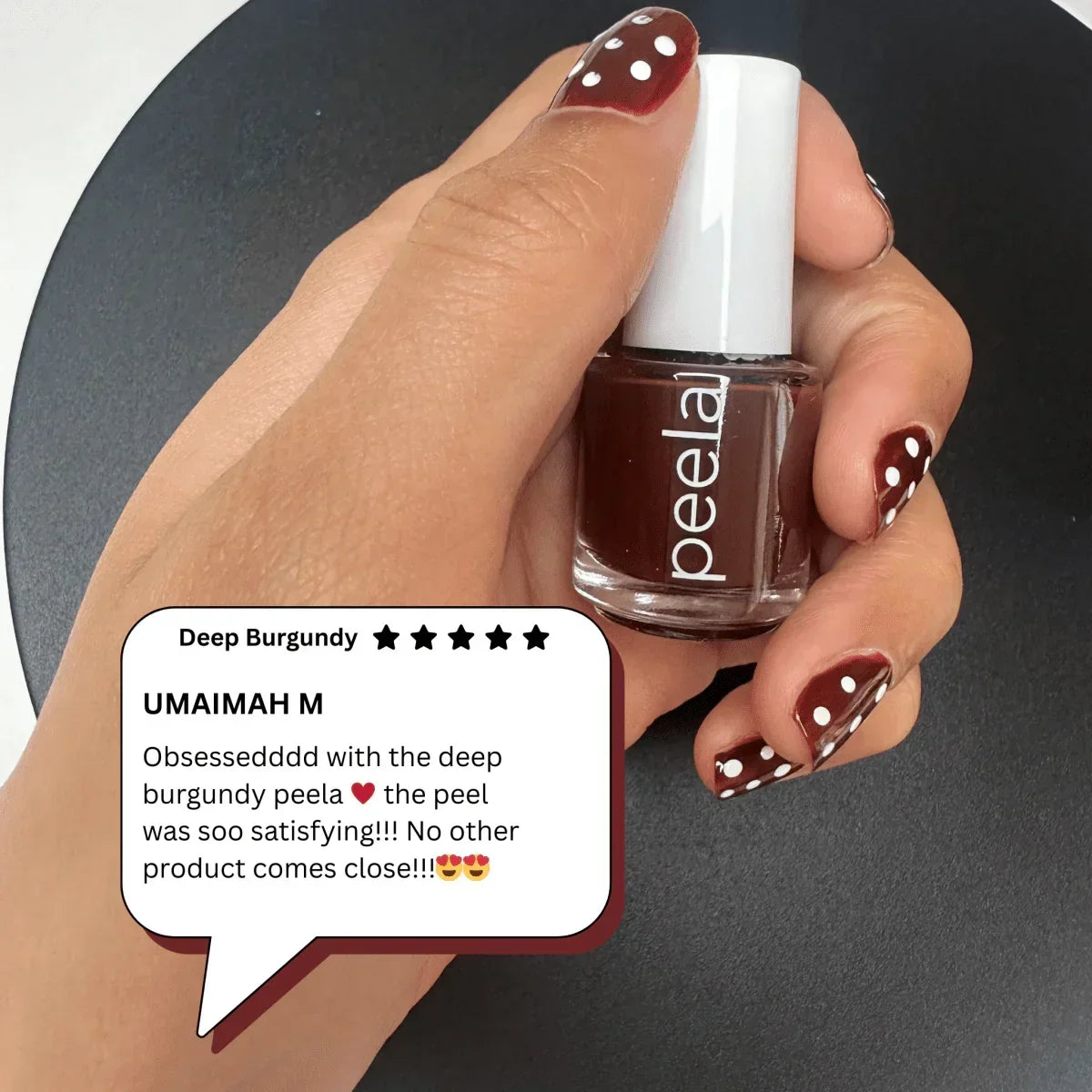 Hand holding peelanails deep burgundy peelable nail polish, nails painted with burgundy and white dots.